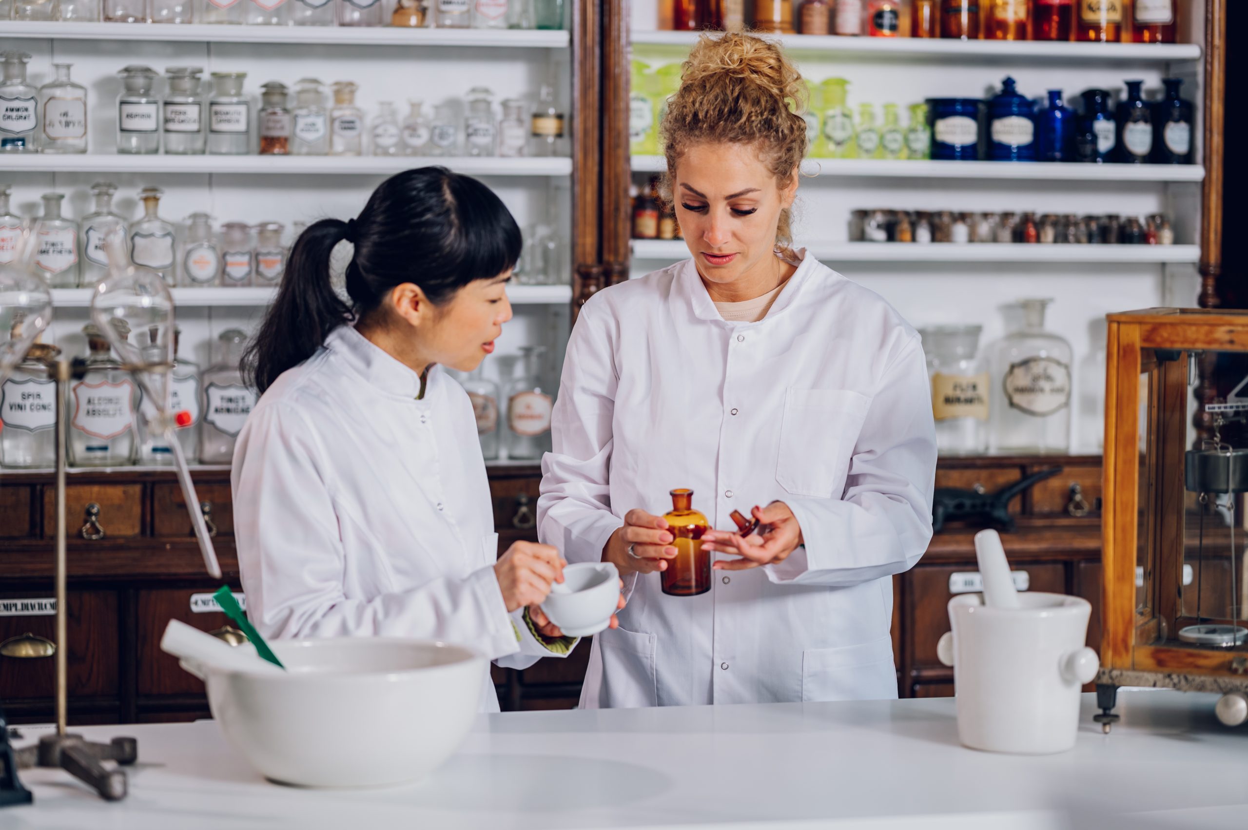 Une chimiste japonaise mélange et prépare des médicaments dans un mortier tandis que son assistant ajoute un ingrédient liquide dans un apothicaire. Deux pharmaciens multiraciaux fabriquent des médicaments ensemble dans une pharmacie.<br />
